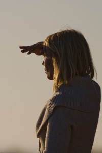 Beautiful blond lady shields her eyes from the setting sun in golden late light.